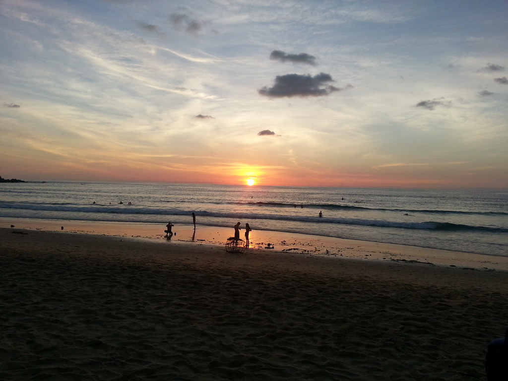 Sunset over Karon Beach in Phuket with people silhouetted at the waterline