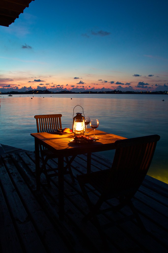 A candlelit dinner table with lanterns overlooking the sea at sunset