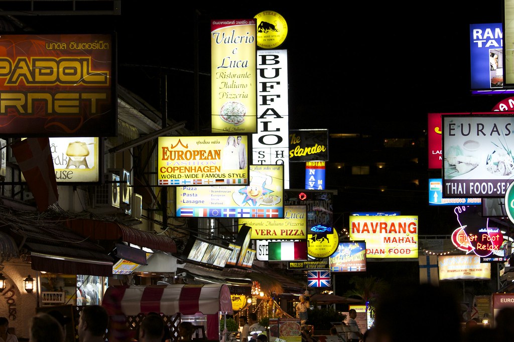 Illuminated restaurant and bar signs stacked above a Patong street at night