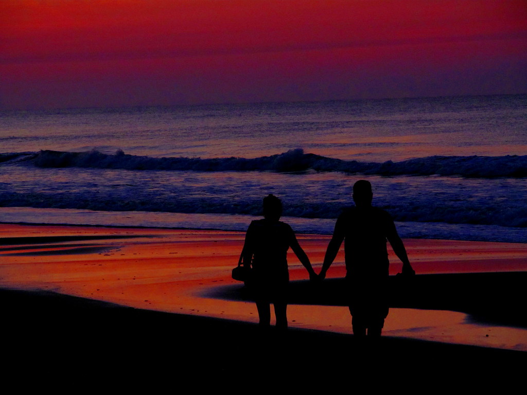 A couple walking hand in hand along a Phuket beach at sunset