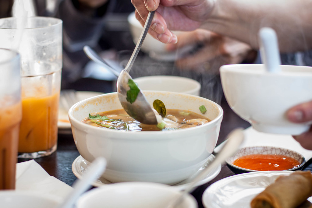 Bowl of tom yum being served at a Thai restaurant table with iced tea and spring rolls